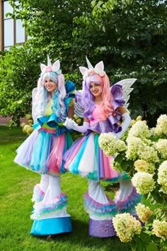 two women dressed in colorful costumes standing next to each other on the grass with flowers