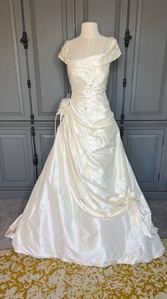 a white wedding dress is on display in front of a gray wall and yellow carpet