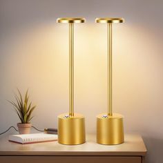 two golden lamps sitting on top of a wooden table next to a potted plant