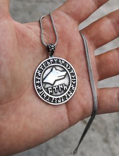 a hand holding a silver pendant with an image of a dinosaur in it's center