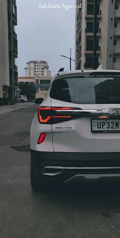 the rear end of a white car parked in front of tall buildings