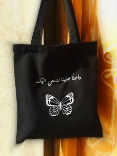 a black tote bag with white butterflies on the front and arabic writing on the back