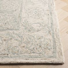 a white rug with an intricate design on the top and bottom corner, laying on a wooden floor