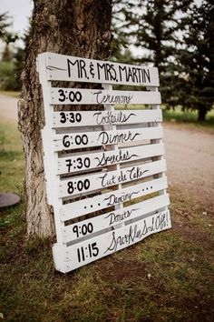 a sign that is sitting in the grass near a tree with writing on it's side