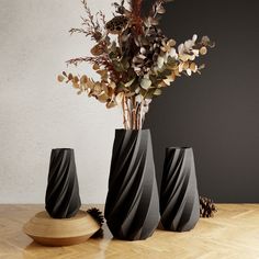 three black vases sitting on top of a wooden table next to a flower arrangement