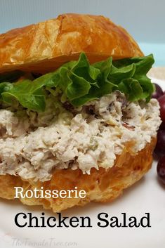 a chicken salad sandwich with lettuce and grapes on a white plate next to croissants