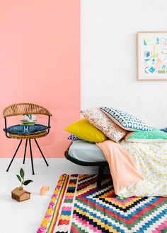 a bed with colorful pillows and blankets on top of it next to a small chair