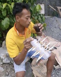 a man sitting on the ground holding a cup with toothpicks stuck in it