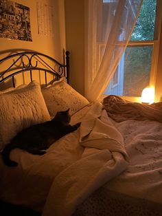 a black cat laying on top of a bed next to a night stand and window