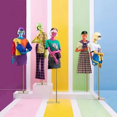 three mannequins dressed in brightly colored clothing stand on metal poles against a multicolored wall