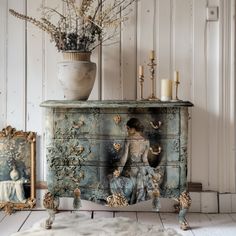 an antique chest with pictures on it and candles in the background, next to a potted plant