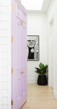 an open door leading to a white room with a plant in the corner and a framed photograph on the wall