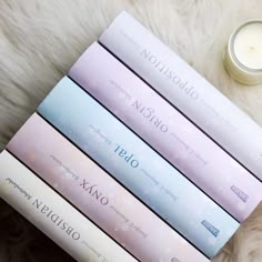 four books sitting on top of a white fur covered floor next to a lit candle