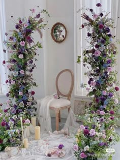 an arrangement of flowers and greenery is arranged around a chair in front of two windows