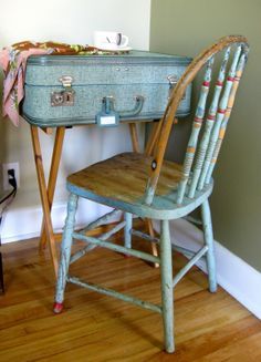 an old blue suitcase sitting on top of a wooden desk next to a chair and table