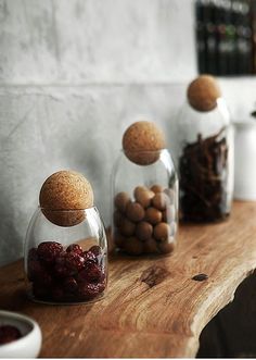 three glass jars filled with nuts and chocolates on a wooden table next to a white wall