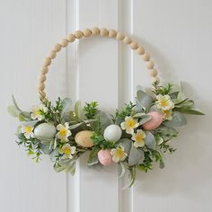 a wreath with flowers and eggs hanging on a door