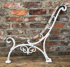 an old white iron bench against a brick wall in front of a wood flooring board