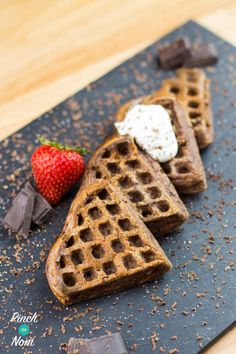 chocolate waffles with whipped cream and strawberries on a black slate platter