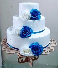 three tiered wedding cake with blue and white flowers on top, sitting on a table