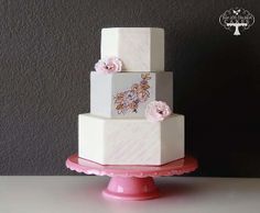 a three tiered white and pink cake with flowers on the top is sitting on a table