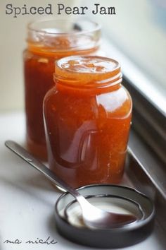 two jars filled with jam sitting on top of a counter next to a spoon and window sill