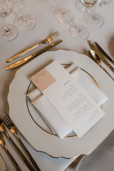 a place setting with silverware and napkins on a white table cloth, along with gold cutlery