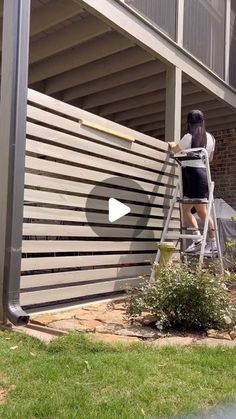 a woman is painting the side of a building with a paint roller and a ladder