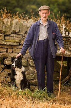 an old man standing next to a dog with a stick in it's mouth