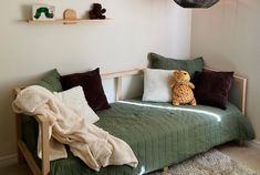 a green daybed with pillows and a stuffed animal sitting on top of the bed