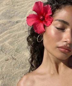 a woman with a flower in her hair laying on the sand and looking off into the distance