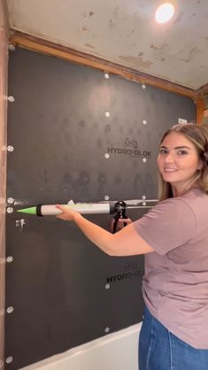 a woman holding a baseball bat in front of a wall with drywalling on it