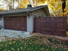 a house with two brown garage doors in front of it and leaves on the ground