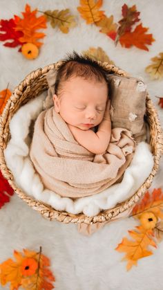 a newborn baby wrapped in a blanket is laying in a basket with fall leaves around it