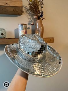 a person's hand holding up a silver disco ball hat on top of a mirror plate