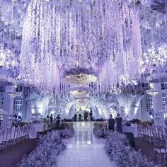 an indoor wedding venue with purple flowers and chandeliers hanging from the ceiling above