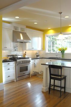 a kitchen with yellow walls and white cabinets is pictured in this image, there are two chairs at the center of the island