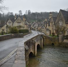 an old stone bridge over a river in the middle of a village with houses on either side