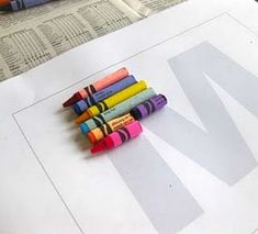 some crayons are laying on top of a piece of paper with the letter m next to them