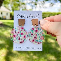 a person holding up a pair of flowery earrings in front of a house and grass