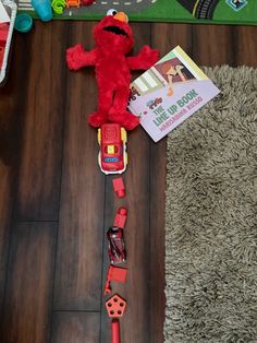 a red stuffed animal laying on top of a wooden floor next to a book and toys