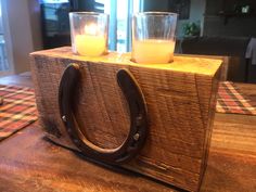 two candles sitting on top of a wooden block with a horseshoe shaped candle holder next to it