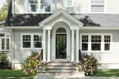 a white house with flowers in the front yard and steps leading up to it's entrance