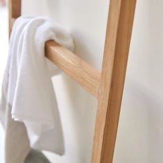 a towel hanging on the side of a wooden ladder next to a white bed sheet