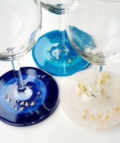 three wine glasses sitting next to each other on top of a white table with gold flakes all over them