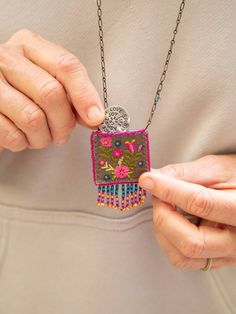 a woman is holding a necklace with flowers on it and a medallion hanging from the chain