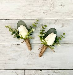 two boutonnieres with white flowers and greenery on top of wood planks