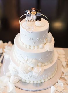 a three tiered wedding cake decorated with sea shells and small figurines on top