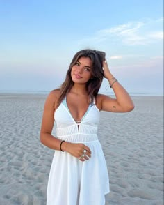 a woman standing on top of a sandy beach wearing a white dress and bracelets