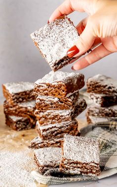 a hand is picking up some brownies from a stack